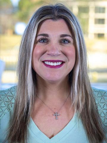A portrait of Krystal Tosch. She smiles as she looks directly into the camera. She has long hair and is wearing a robin's egg blue shirt.